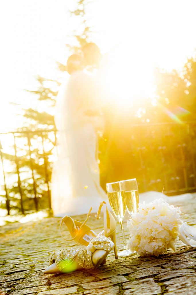 golden hour shot mit brautpaar im hintergrund und blumenstrauss und schuhen im Vordergrund