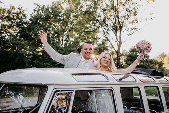 hochzeitspaar auch aus einem VW Bus Auto aus dem Dach heraus und winkt